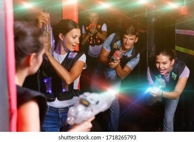 Portrait of happy cheerful glad friends playing laser tag  game  with laser guns in dark corridor