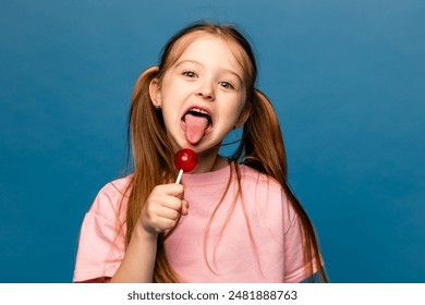 Portrait of happy cheerful little girl lick chupa-chups candy enjoy sweet snack wear good look clothes isolated over blue color background