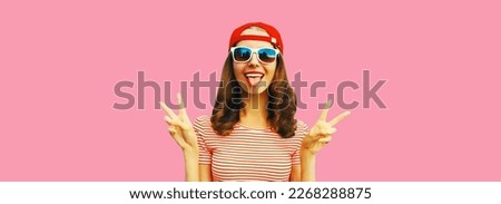 Portrait of happy cheerful smiling young woman having fun showing her tongue wearing red baseball cap on pink background