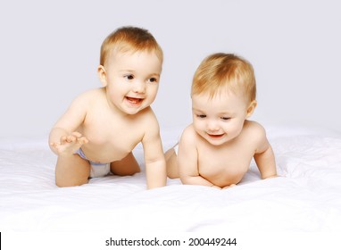 Portrait of happy cheerful two twin babies crawling and playing on the bed on white background