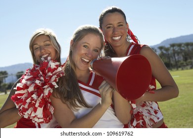 Portrait Of Happy Cheerleader Holding Megaphone With Friends