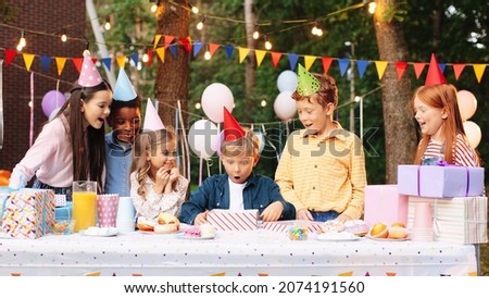 Portrait of happy child boy having fun to opening present at the table with his friends. Concept of surprise present, birthday gift, happy kids, childhood 