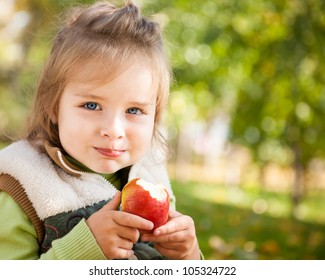 Portrait Of Happy Child Eating Red Apple Outdoors In Autumn