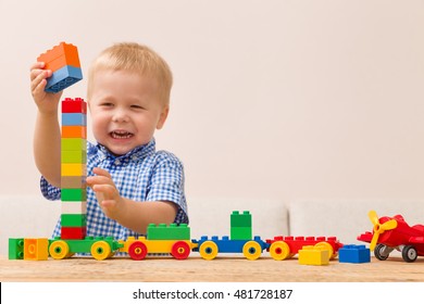 Portrait Of Happy Child Playing With Colorful Plastic Bricks At The Table. Toddler Having Fun And Building A Train Out Of Constructor Bricks. Early Learning. Developing Toys