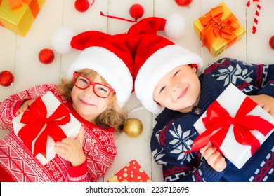 Portrait Of Happy Children With Christmas Gift Boxes And Decorations. Two Kids Having Fun At Home