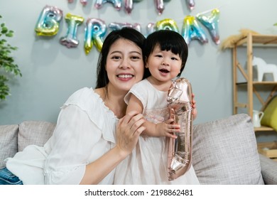 Portrait Of A Happy Chinese Mom Holding Her Cute Baby Child And Looking At The Camera With Smile In A Birthday Party At Home