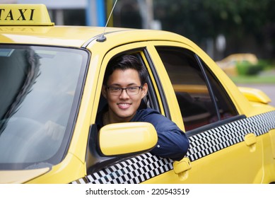 Portrait of happy chinese taxi driver in yellow car smiling and looking at camera