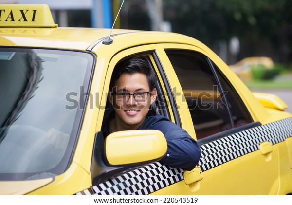 Portrait of happy chinese taxi driver in yellow\
car smiling and looking at\
camera