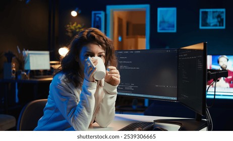 Portrait of happy computer engineer enjoying hot tea while implementing security measures to protect company systems and data. Joyful IT worker holding coffee mug and debugging code, camera B - Powered by Shutterstock