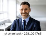 Portrait of happy confident middle aged businessman in suit looking and smiling at camera, posing in office interior, free space. Ceo manager and boss, successful work, career concept