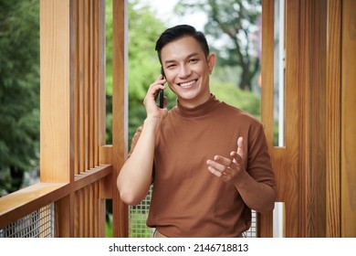 Portrait Of Happy Confident Young Man Standing On Apartment Balcony And Calling Friend To Discuss Latest News