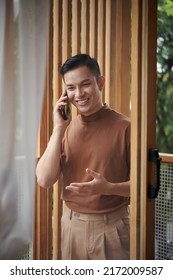 Portrait Of Happy Confident Young Man Standing On Apartment Balcony And Calling Friend To Discuss Latest News