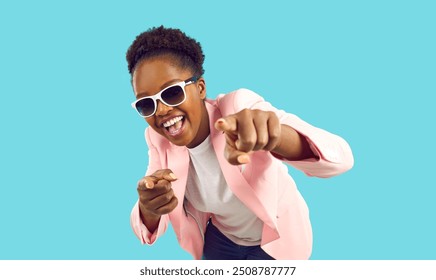 Portrait of happy confident young woman in stylish party outfit. Positive beautiful African American lady wearing fashionable pink suit and cool sunglasses looking at camera, smiling and pointing at - Powered by Shutterstock