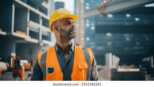 Portrait of Happy Construction Worker Carrying a Theodolite, Posing for Camera. Professional Heavy Industry Engineer Wearing Safety Orange Uniform and Protective Hard Hat