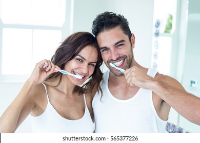 Portrait of happy couple brushing teeth in bathroom at home
