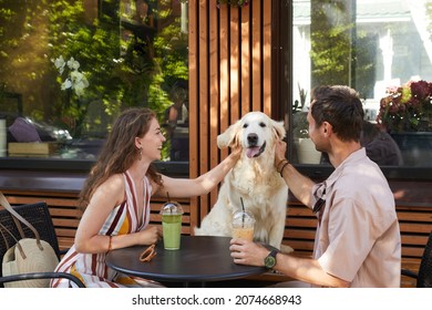 Portrait Of Happy Couple With Dog Sitting At Table Together In Outdoor Cafe And Laughing, Copy Space