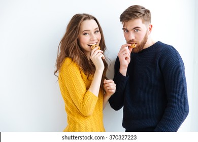 Portrait of a happy couple eating cookies over white background and looking at camera