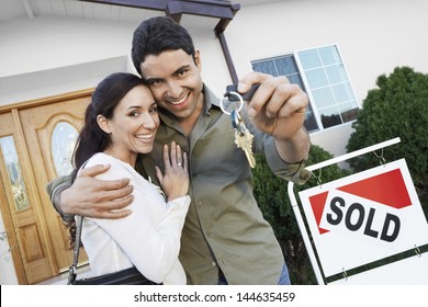 Portrait Of A Happy Couple Holding Keys In Front Of Their House By Sold Sign