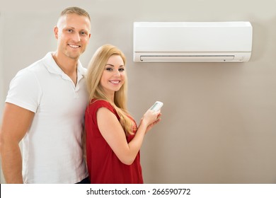 Portrait Of Happy Couple Holding Remote Control Air Conditioner