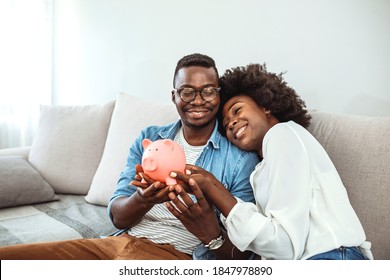 Portrait Of A Happy Couple At Home Saving Money In A Piggybank. Portrait Of A Happy African American Couple At Home Saving Money In A Piggybank And Smiling