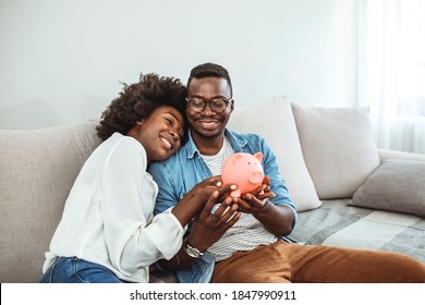 Portrait of a happy couple at home saving money in a piggybank. Portrait of a happy African American couple at home saving money in a piggybank and smiling