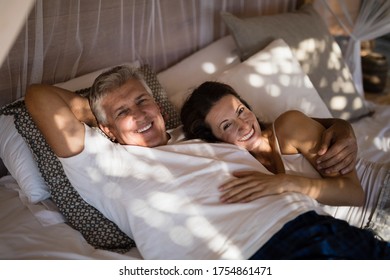 Portrait of happy couple relaxing in canopy bed during morning