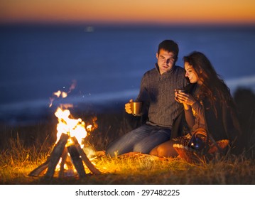 Portrait of the happy couple sitting by fire on autumn beach at the night