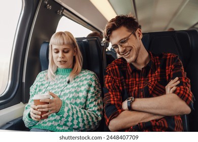 Portrait of a happy couple sitting in a train and talking during journey. A girl is holding coffee to go and talking while a who is sitting next to her is listening and smiling. Traveler in train. - Powered by Shutterstock