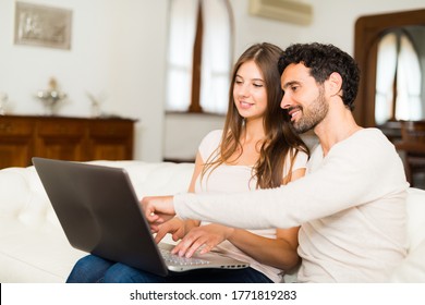 Portrait Of An Happy Couple Using A Laptop Computer In Their House. Shallow Depth Of Field, Focus On The Man