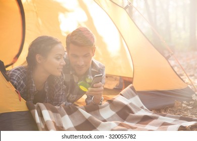 Portrait of a happy couple using smartphone in the tent outdoors - Powered by Shutterstock