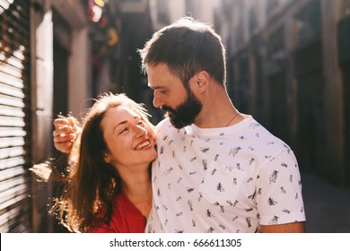 Portrait of a happy couple of young lovers laughing while walking down the street on a sunny summer day. A man looks at his girlfriend while standing on an urban background. Romantic dating.