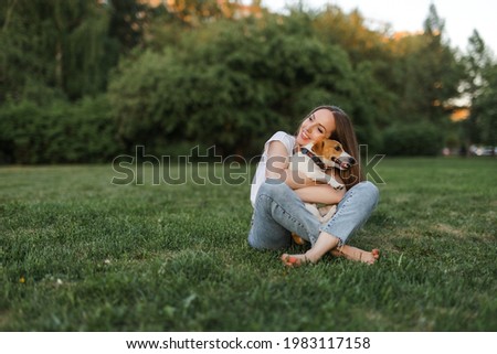 Portrait of a happy and crazy Jack Russell Terrier dog. Smooth coat of red color. a girl with brown hair in jeans and a T-shirt is playing with a dog. Cute and beautiful dog has fun outdoors.