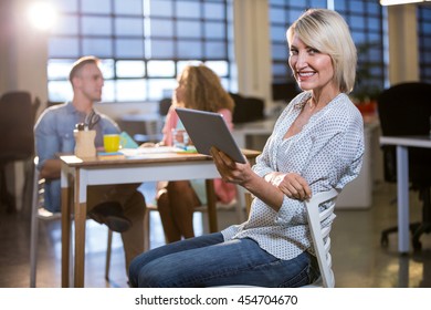 Portrait of happy creative businesswoman using digital tablet while sitting in office - Shutterstock ID 454704670