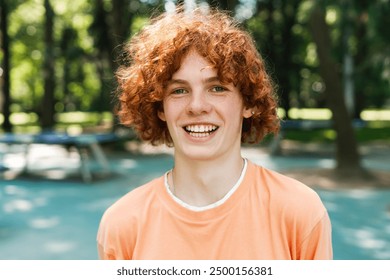 Portrait of happy curly red hair teenager boy looking at camera posing in the park. Lifestyle emotions concept - Powered by Shutterstock