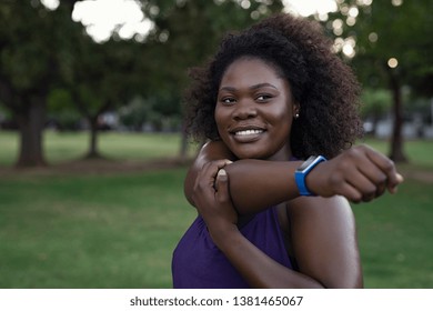 Portrait of happy curvy african woman stretching arms in park. Confident oversize young woman with curly hair smiling while exercising outdoor. Sporty african american girl training outdoors. - Powered by Shutterstock