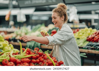 Portrait of a happy customer choosing and buying fresh organic vegetables at food market. Smiling shopper woman picking fresh vegetables from market stall at farmers market and buying organic produce. - Powered by Shutterstock