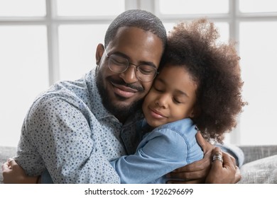 Portrait Of Happy Cute Black Girl Hugging Her Beloved Daddy And Smiling With Closed Eyes. Peaceful Affectionate Dad And Daughter Kid Enjoying Time Together, Embracing, Relaxing At Home. Close Up