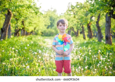 Portrait Of A Happy Cute Little Boy Holding Pinwheel At The Park. Kid Hold In Hand Play With Windmill. Boy Smiling In Spring Or Summer Forest. Outdoors Leisure Friendship Family Concept.