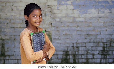 Portrait of happy cute little indian girl in school uniform holding blank slate, Adorable elementary kid showing black board. child education concept. rural india.