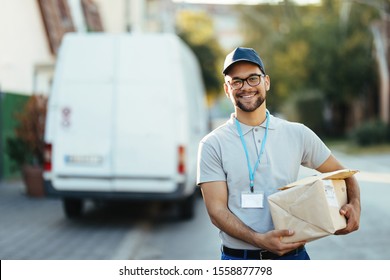 Portrait Of Happy Delivery Man Carrying Packages And Looking At Camera While Standing On The Street. 