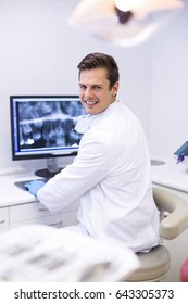 Portrait Of Happy Dentist Examining X-ray Report On Computer In Clinic