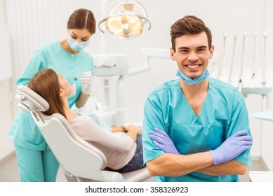Portrait of a happy dentist in a mask and gloves on the background of the assistant who treats teeth patient