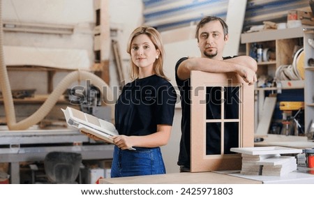 Portrait happy designer with color sample project and carpenter man with wooden furniture in workshop. Kitchen cabinet renovation and design concept.