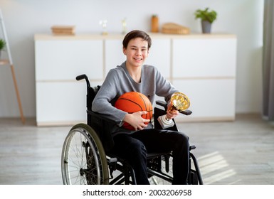 Portrait of happy disabled teen in wheelchair holding basketball and prize, smiling at camera indoors. Joyful impaired teenage sportsman winning championship, celebrating his victory - Powered by Shutterstock