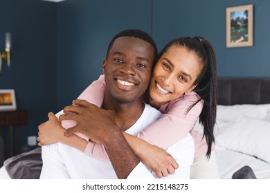 Portrait Of Happy Diverse Couple Embracing Sitting On Bed Smiling To Camera At Home. Happiness, Domestic Life, Love And Inclusivity Concept.