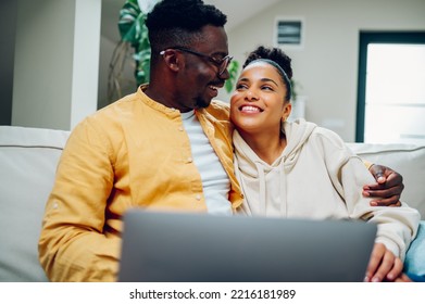 Portrait Of A Happy Diverse Couple Relaxing At Home And Using Laptop Together. Smiling African American Husband And Hispanic Wife Spending Time Together On A Couch And Looking At Each Other.