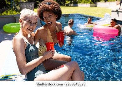 Portrait of happy diverse female friends having pool party, embracing and smiling in garden. Lifestyle, friendship, party and summer. - Powered by Shutterstock