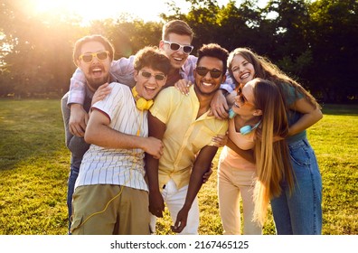 Portrait of happy diverse friends having fun on warm sunny evening in summer park. Bunch of cheerful young people standing on green lawn, smiling and posing for funny group photo together