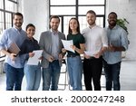 Portrait of happy diverse group of interns or students and corporate teacher after successfully passes exam. Multi ethnic business team of employees holding paper documents, looking at camera, smiling