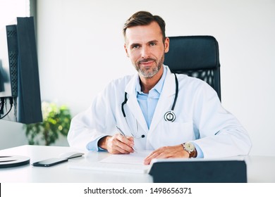 Portrait Of Happy Doctor Looking At Camera While Filling Out Paperwork Between Patients